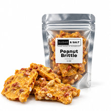 Load image into Gallery viewer, Sugar &amp; Salt Peanut Brittle in a silver resealable 2oz pouch with several pieces of golden-brown brittle and peanuts in front on a white background.