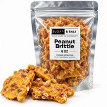 Load image into Gallery viewer, Sugar &amp; Salt Peanut Brittle in a silver resealable 8oz pouch with several pieces of golden-brown brittle and peanuts in front on a white background.