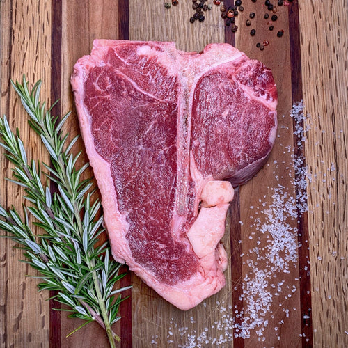 Foggy Bottoms Boys T-Bone Steak on wooden cutting board with salt, pepper corns and rosemary